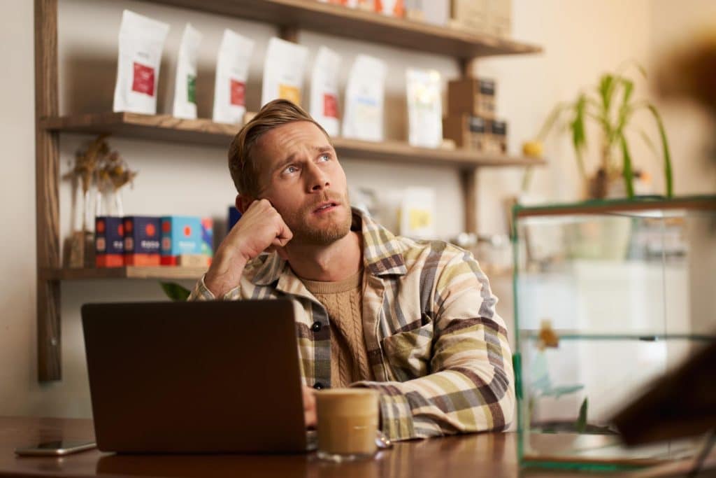 Person working in a café on laptop, stuck doesnt know what to do